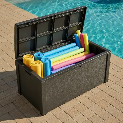 A spacious extra-large resin deck box filled with colorful deflated and rolled pool floats and pool noodles next to a sunny swimming pool patio.
